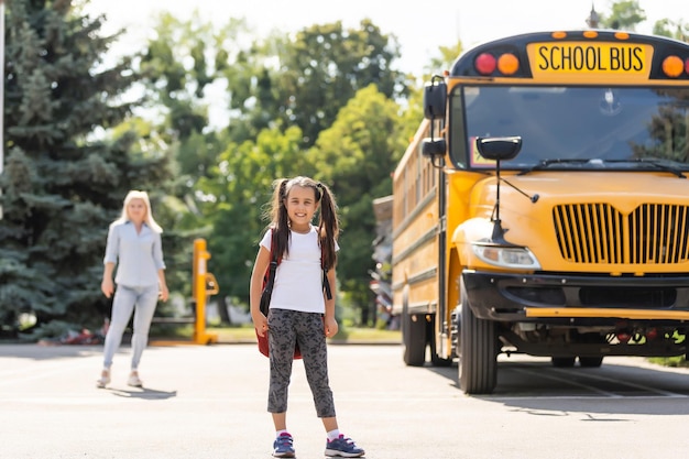 Photo mother escorts the schoolgirl with ponytails and a backpack to school.