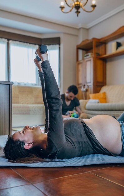 Mother exercising while father playing with son in background at home