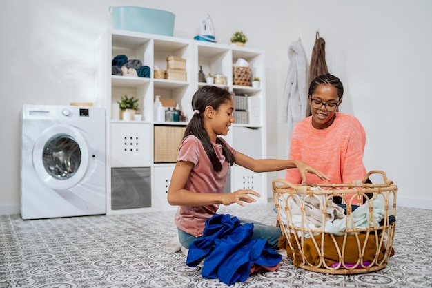 The mother explains to daughter how to sort laundry explains\
the operation of the washing machine the woman and girl sit on\
floor by a large wicker basket with clothes they take out colorful\
things