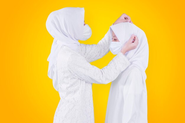 Mother in face mask tidying veil of her daughter