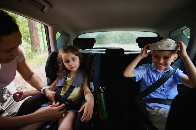 かわいい娘を車内のチャイルドシートに固定する母親。車内の安全ブースターチャイルドシートの子供たち
