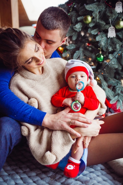 The mother,father and baby sitting near Christmas Tree