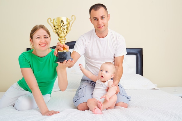 Foto madre padre e bambino con il campione della coppa sul letto insieme il concetto di una super famiglia e di super eroi