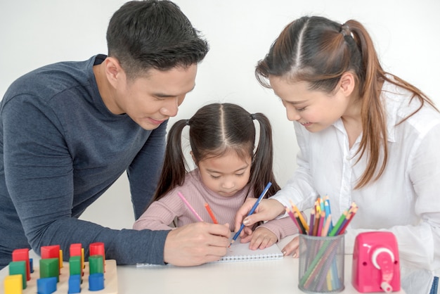 Mother and father help their daughter do homework in living room