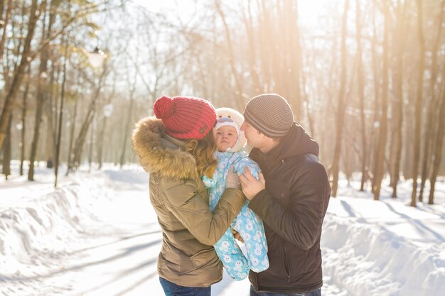 Mother and father holding their baby boy and kissing his outside in the winter.