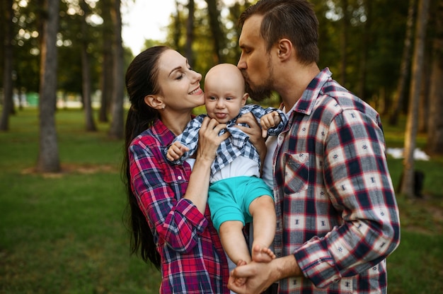 Mother and father kissing their little baby in summer park