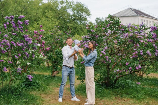 Photo mother father and little son are walking in a spring blooming park a happy mom and dad with a small child are having fun near the lilac the concept of a happy family