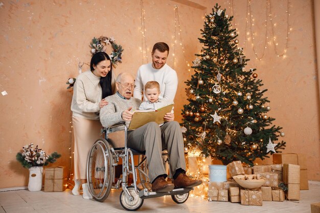 Mother father little son and old grandfather on a wheelchair sitting near Christmas tree