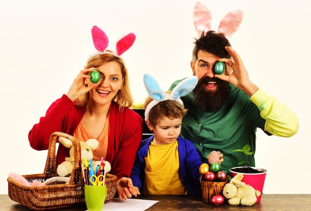 Madre, padre e figlio con le orecchie da coniglio si siedono al tavolo di legno famiglia felice che celebra il giorno di pasqua