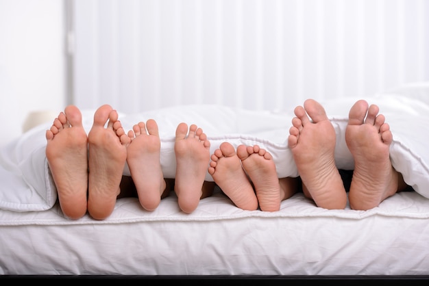 Mother, father and two children lie on bed with white sheets