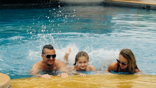 The mother and father with little daughter have fun in the pool Mom and dad plays with the child The family enjoy summer vacation in a swimming pool jumping spinning splash water Slow motion