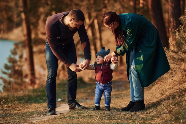 Mother and father with their little son have a walk in spring forest at daytime