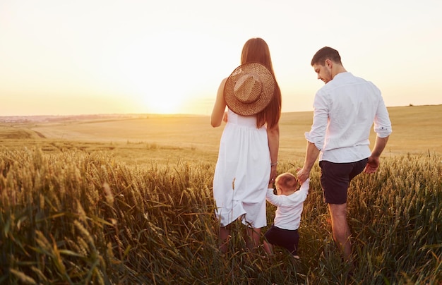 Mother and father with their son spending free time on the field at sunny day time of summer View from behind