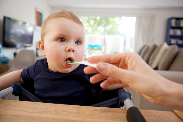 Mother feeding baby with spoon at home