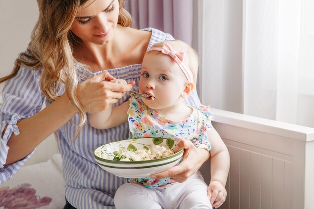 Photo mother feeding food to cute baby at home