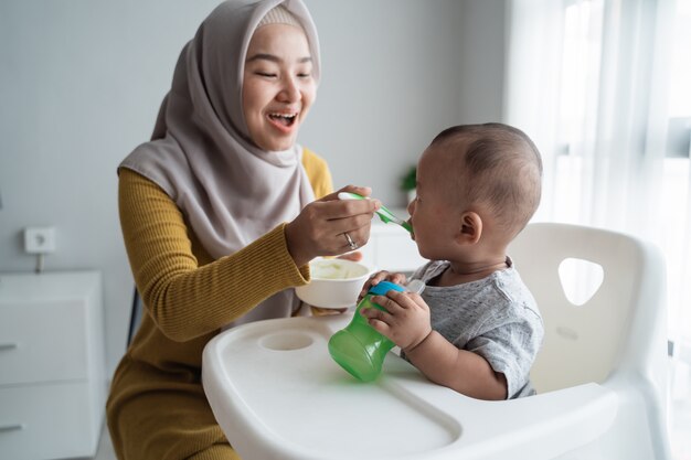 Mother feeding her baby boy while sitting on high chair