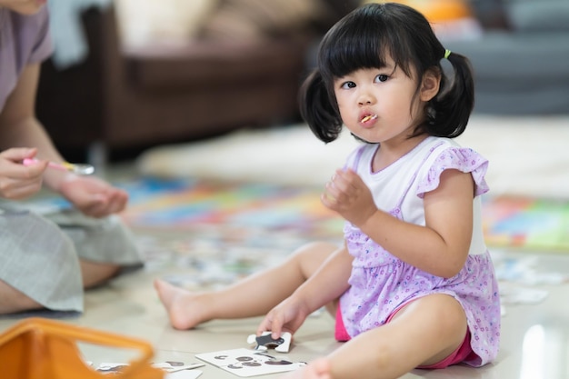 母は彼女の赤ん坊の娘を養うリビングルームで母と食事を食べる幸せな女の赤ちゃん