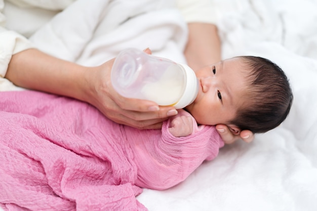 Mother feeding milk bottle to her newborn baby on a bed