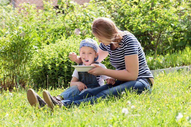 Photo mother feeding son while sitting grassy field