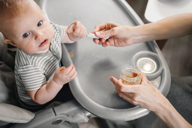 Mother feeding with vegetables or fruits pure baby on highchair