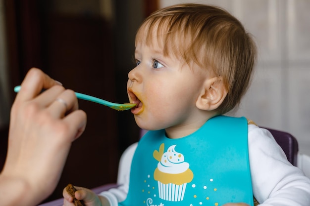 The mother feeds the baby at the table with a spoon