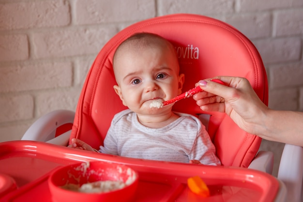 A mother feeds her discontented child with a spoon .