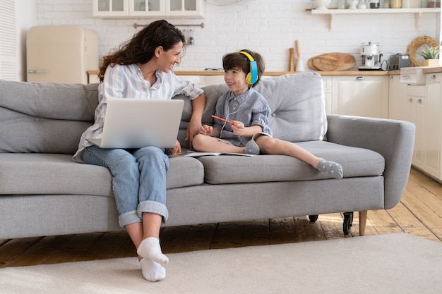 Mother freelancer enjoy helping little son with homework distance lessons as work remotely from home