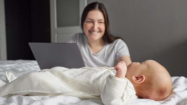 Mother freelancer looks after baby girl working on laptop