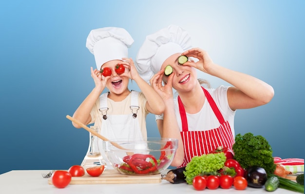 Mother and funny daughter playing in the kitchen with vegetables