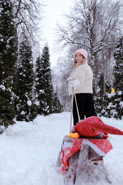 Mother or girl or woman walking in the forest in winter with sledges and white winter landscape on background