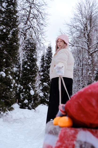 Mother or girl or woman walking in the forest in winter with sledges and white winter landscape on background