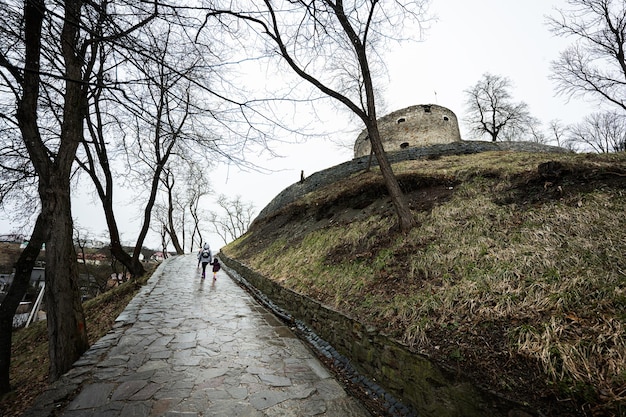 Mother and girls walk up the wet path to an ancient medieval castle fortress in rain