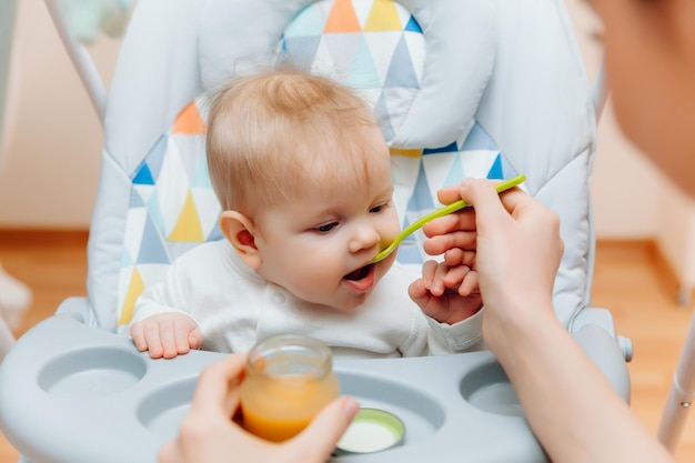 Photo mother gives fruit sauce to babymom feeds baby on highchairbaby food