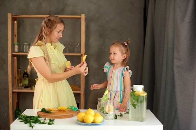 Mother gives lemon slices to little daughter in kitchen family cooking lemonade at home