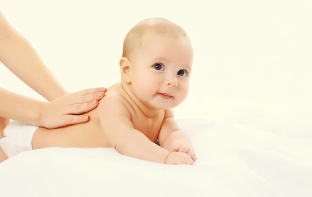 Mother gives massage to baby lying on the bed on white background