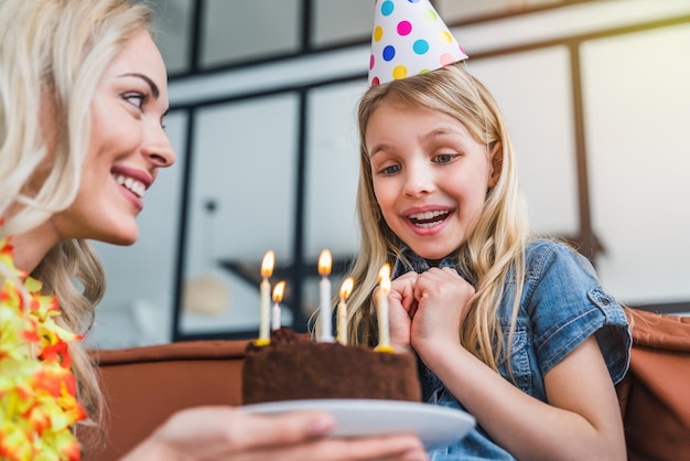 Mother giving birthday cake with candles to funny little girl
at home