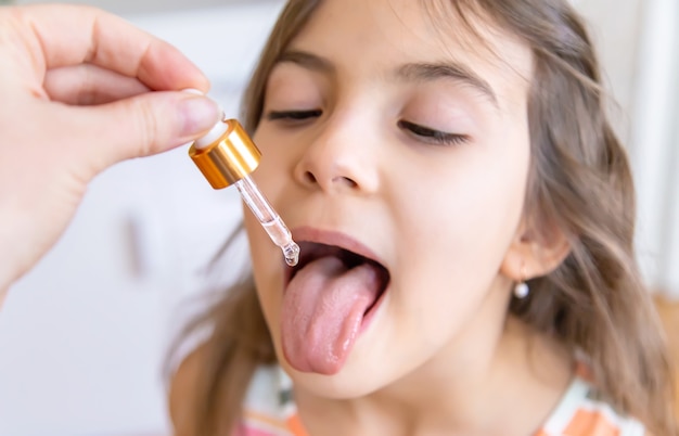 Mother giving vitamin drops with dropper to her child. dietary supplements for kids. Selective focus.