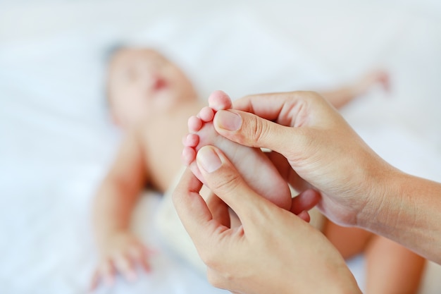 Mother hand massaging feet of infant baby on the bed at home.