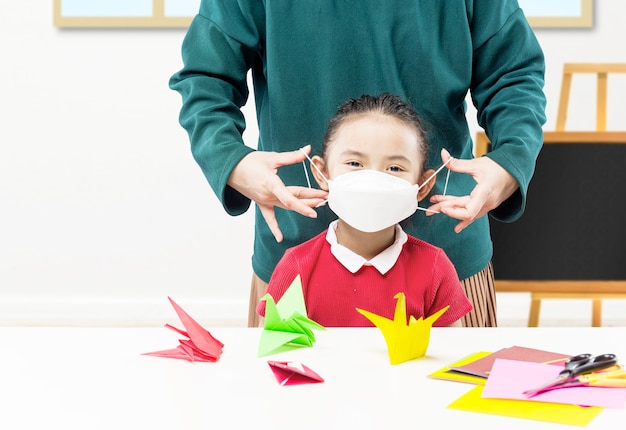 Mother hand putting the mask on her daughter in the classroom