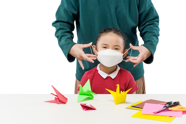 Mother hand putting the mask on her daughter isolated over white background