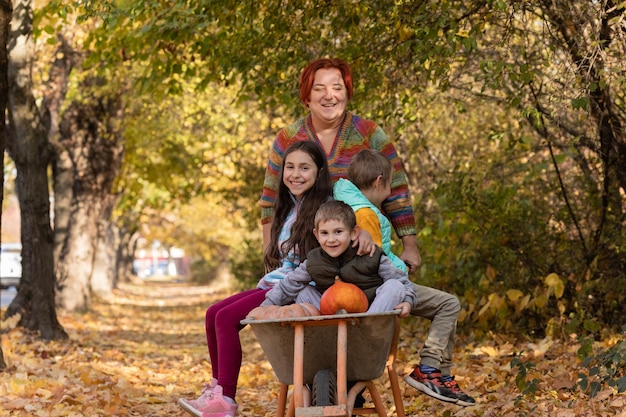 La mamma si diverte con i bambini usa la carriola da giardino con le zucche