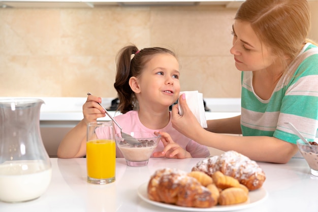 Mother having breakfast with her daughter at a table in kitchen, happy single mother concept