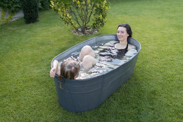 Mother having fun with a child in an outdoor bath tube in the backyard in summertime