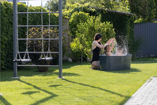 Mother having fun with children in an outdoor bath tube in the backyard in summertime