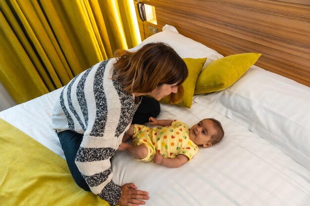 Mother having fun with her baby on the bed in her bedroom, young caucasian first time with her four month old baby