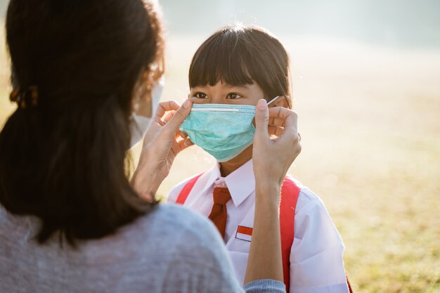 Mother help her daughter to put on the mask before going to school