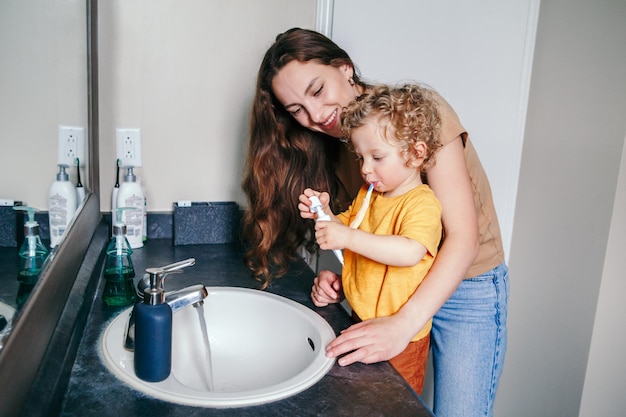 Фото Мать помогает мальчику чистить зубы в ванной комнате дома гигиена здоровья и утренняя рутина