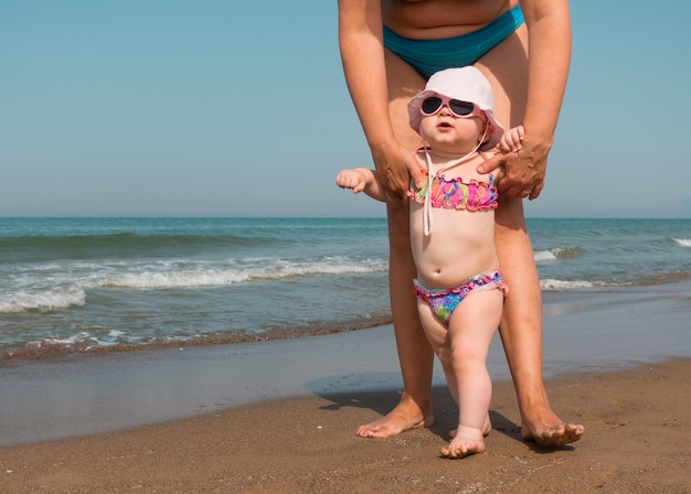Мать помогает ребенку стоять и гулять по пляжу