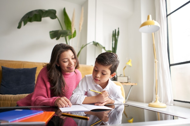 Photo mother helping her son to do homework for school spbi child writing notes in notebook mom helping at...