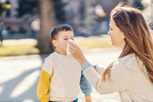 A mother helping son to blow a nose in a park